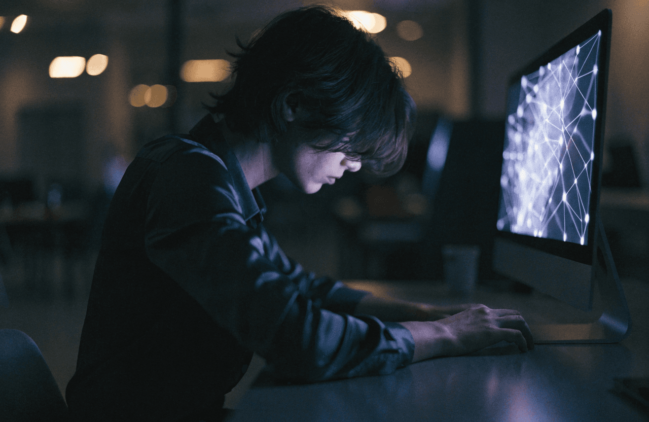 A person working at night with a neural network visualization glowing on screen