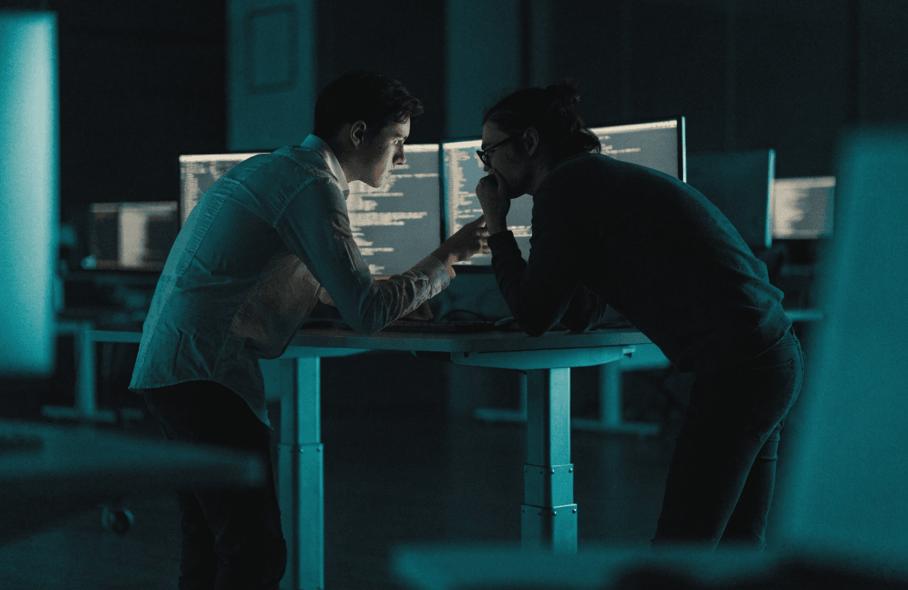 Two software engineers collaborating at a standing desk with code on screen